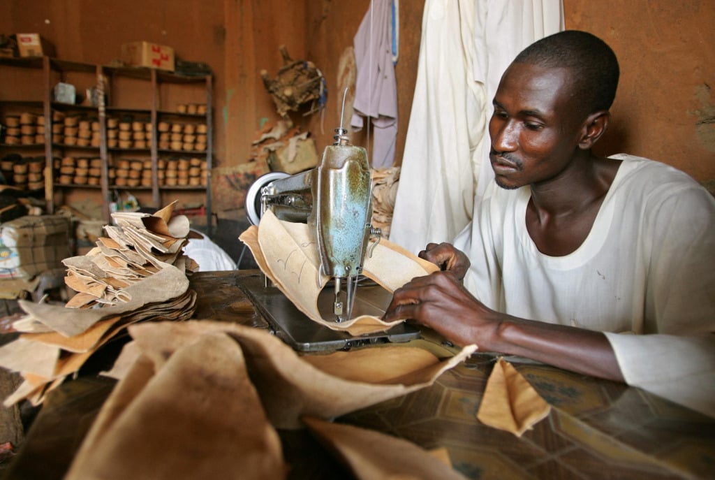 A Sudanese cobbler stitches goat leather shoes.