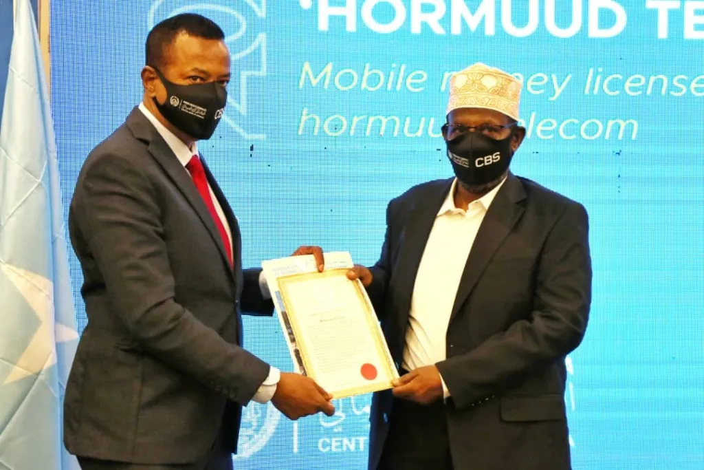 A representative of the Central Bank of Somalia hands a mobile money licence to a representative of Hormuud Telecom.