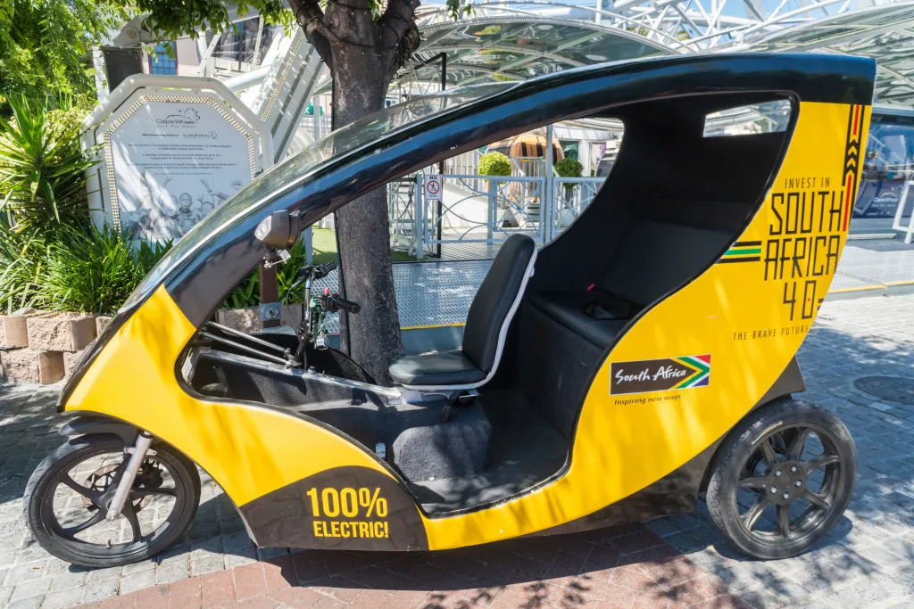 A yellow three wheeled electric vehicle in the shade of a tree at the V&A waterfront in Cape Town, South Africa.