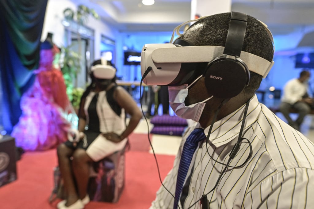 Two Africans in virtual reality headsets, the man in the foreground and the woman sitting in the background.