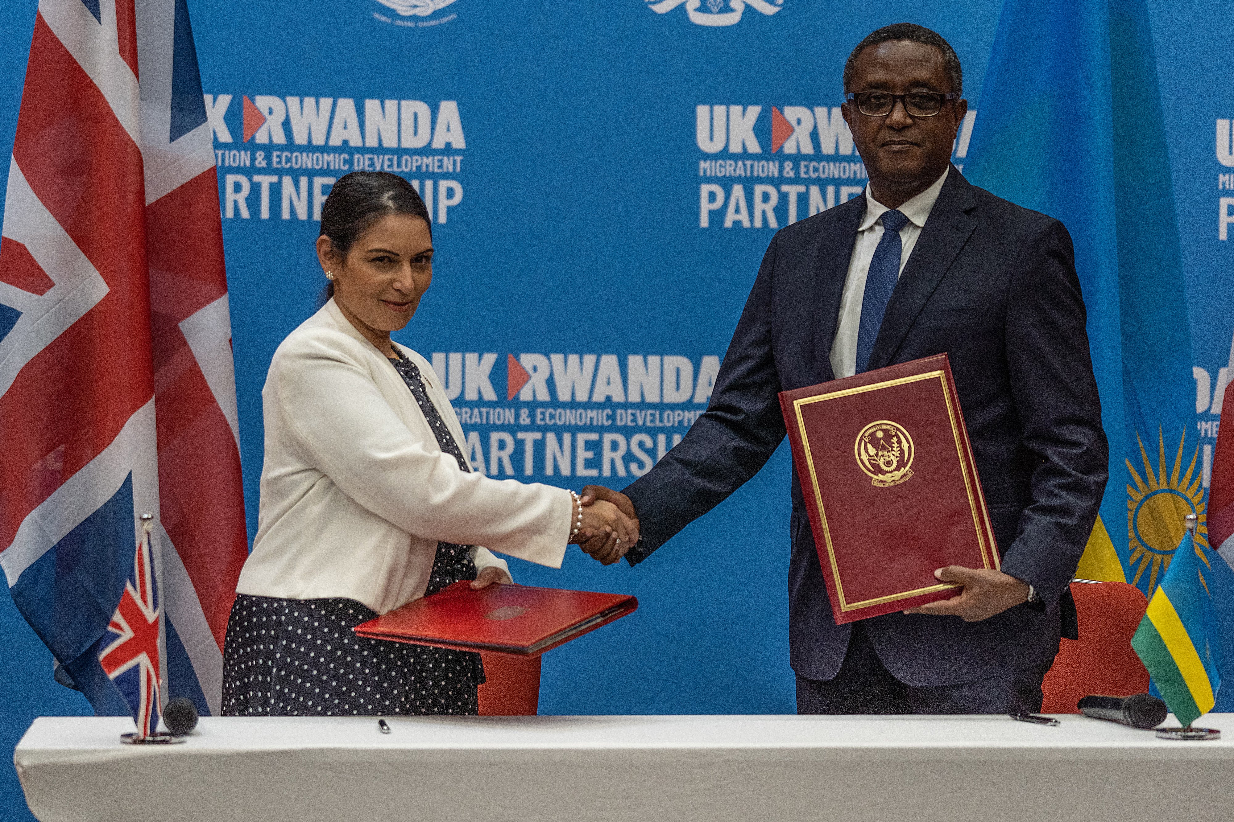 British Home Secretary Priti Patel (L), and Rwandan Minister of Foreign Affairs and International Cooperation Vincent Biruta, shake hands after signing an agreement at Kigali Convention Center, Kigali, Rwanda on April 14, 2022.