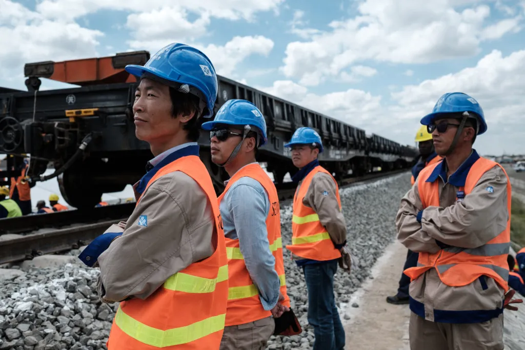 Chinese construction workers standing at the side of a railway track.