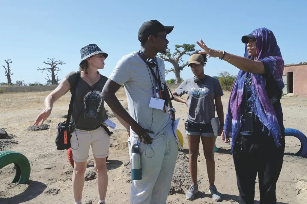 Woman gives directions to film crew against desert background.