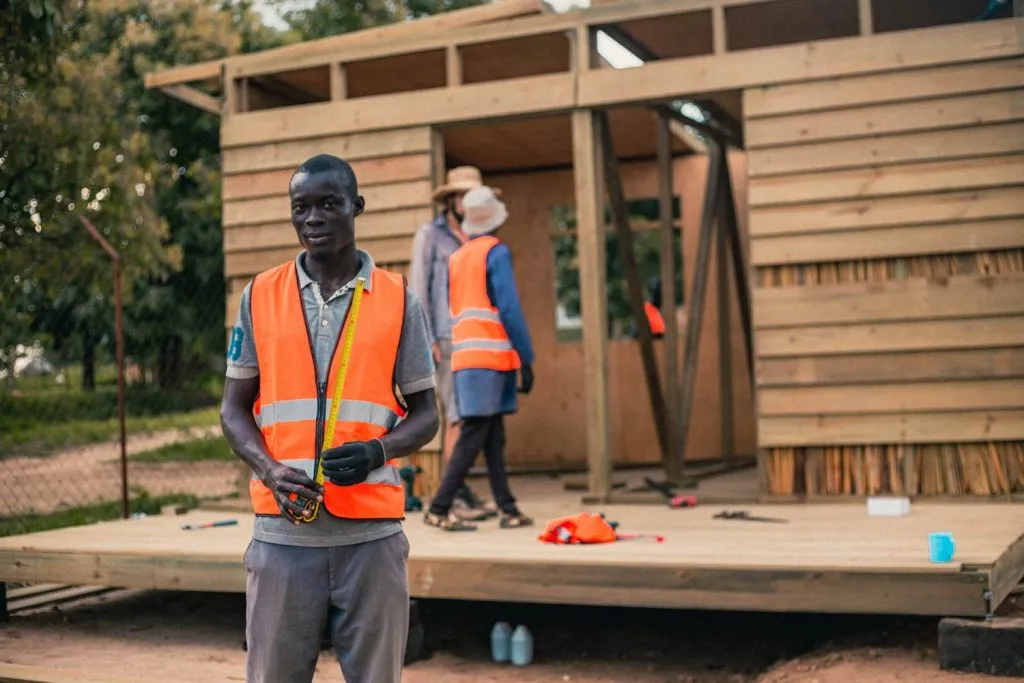 An African builder poses in front of a timber house under construction.