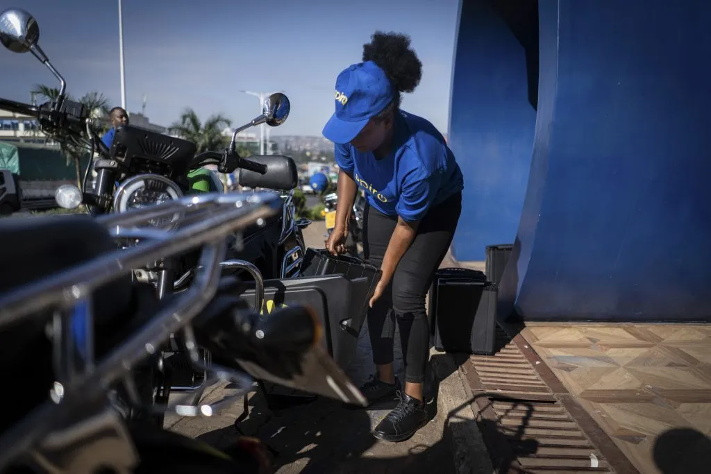 A young woman picks up an electronic battery for a motorcycle.